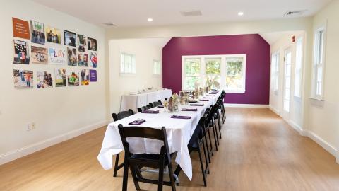 a long table is covered by a white tablecloth and surrounded by black chairs