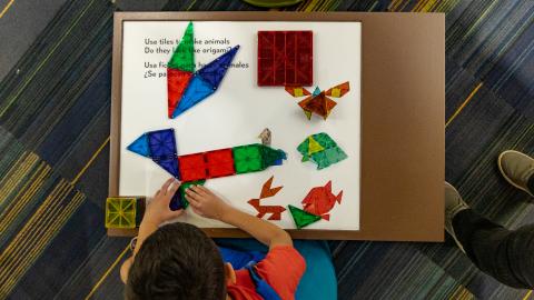 an overhead view of a child working with geometric shapes on a white tabletop