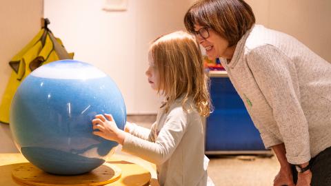 a mom and daughter look at a spinning orb together and discuss