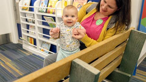 a mother and child sit on a bench near a bookshelf