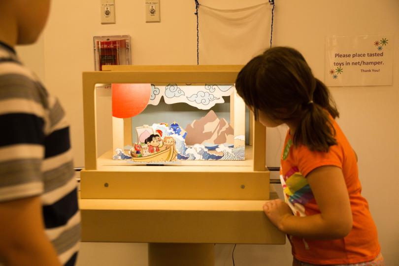 a young girl look into a light-up exhibit of a puppet show