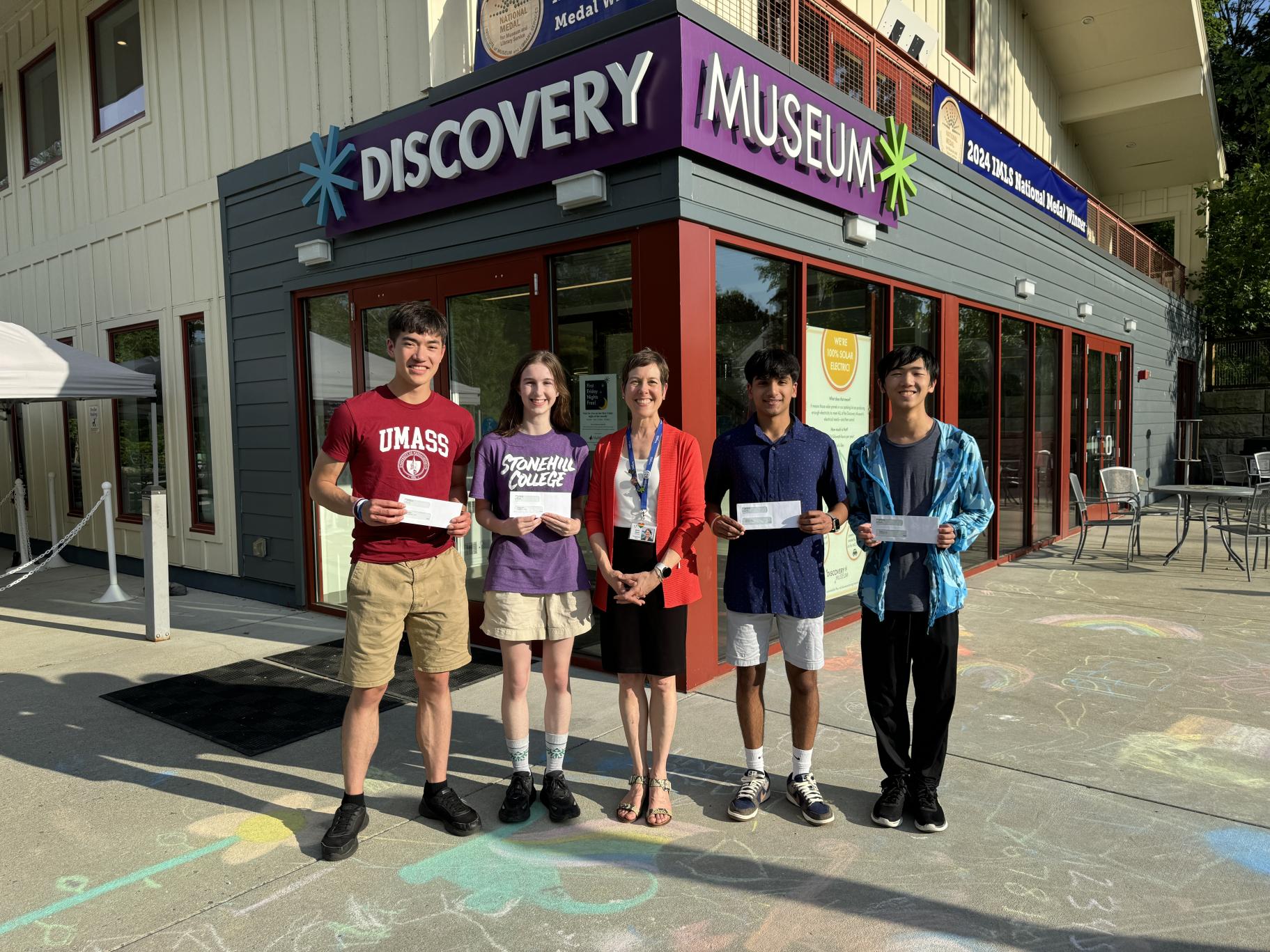 five people stand in front of a museum entrance, four are holding white envelopes