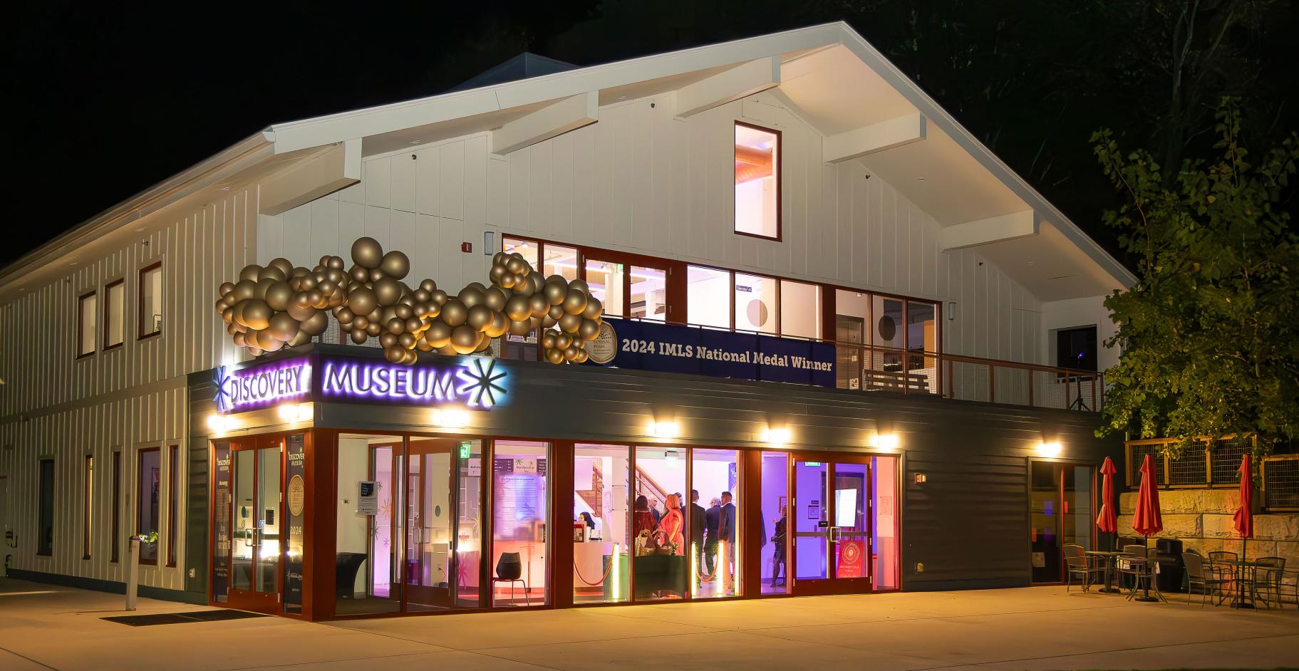 a nighttime photo of a museum building with balloon decorations and event lighting